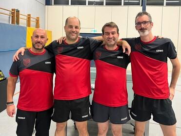 Vier Männer in roten Tischtennis-Trikots stehen nebeneinander, lächeln und umarmen sich in einer Sporthalle.