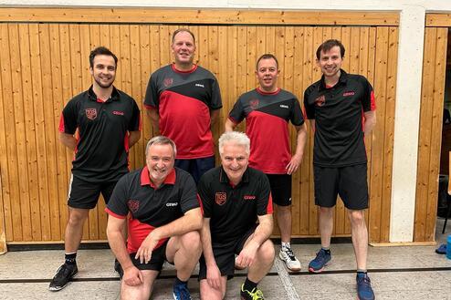 Sechs Männer in Tischtennis-Trikots stehen und sitzen vor einer Holzwand in einer Sporthalle.