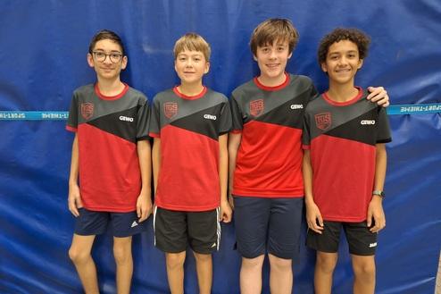 Vier Jungen in roten und grauen Sporttrikots stehen vor einem blauen Hintergrund.