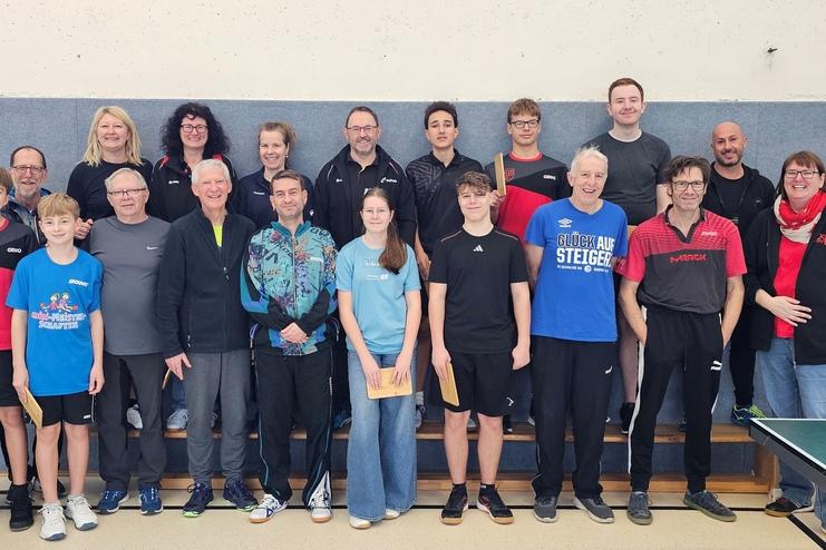 Gruppenfoto von Tischtennisspielern, die auf einer Bühne in Sportbekleidung stehen, lächelnd und posierend.