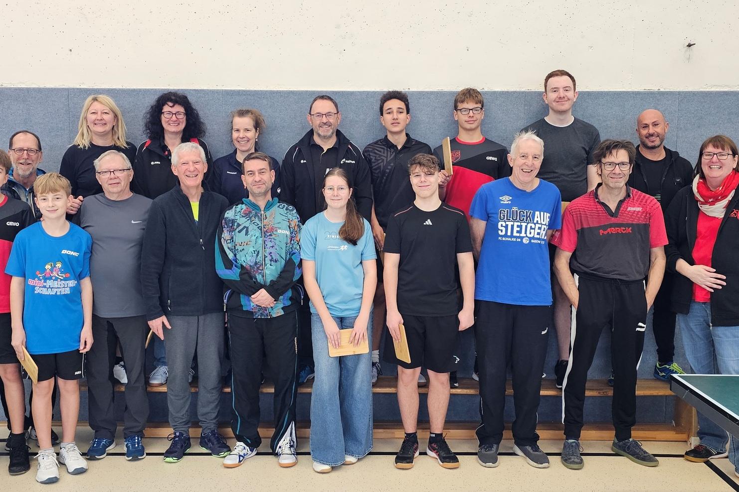 Gruppenfoto von Tischtennisspielern, die auf einer Bühne in Sportbekleidung stehen, lächelnd und posierend.