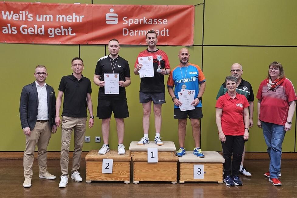 Gruppenbild von Tischtennisspielern auf dem Podium mit Urkunden, nach einem Wettkampf in Darmstadt. Banner im Hintergrund sichtbar.