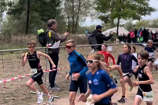 Eine Gruppe von Kindern läuft einen Triathlon-Wettbewerb, umgeben von Zuschauern und Absperrungen.