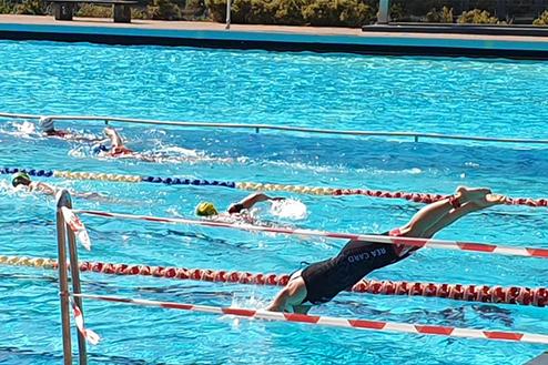 Schwimmer springt ins Wasser eines Außenbeckens mit mehreren Bahnen unter klarem Himmel.