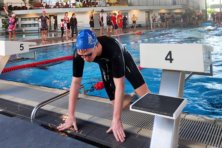 Schwimmer in einem schwarzen Anzug bereitet sich am Startblock auf den Wettkampf in einem Schwimmbad vor.