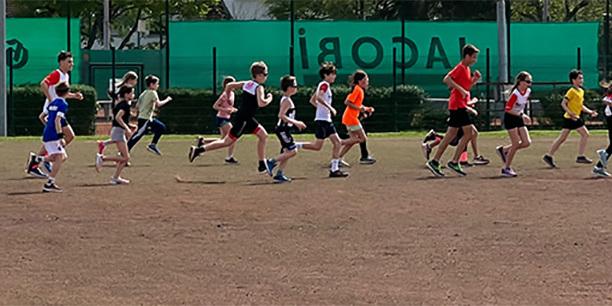 Gruppentraining von Kindern und Jugendlichen auf einem Rasenfeld, die im Lauftempo parallel zueinander laufen.