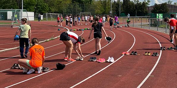 Sportlerinnen und Sportler ziehen sich auf einer Laufbahn um, Schuhe liegen verstreut auf dem Boden.