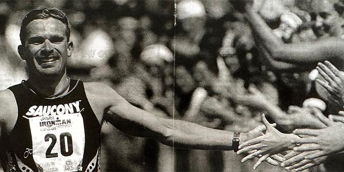Ein Athlet mit der Nummer 20 gratuliert Zuschauern beim Ironman-Wettkampf und reicht ihnen die Hand.