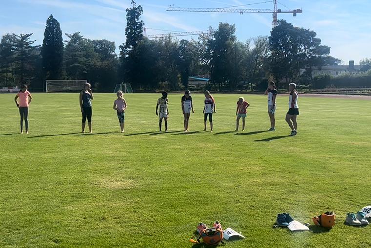 Sechs Kinder stehen auf einem Rasenplatz, neben ihnen liegen verschiedene Sportutensilien und Schuhe.