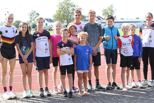 Gruppe von zehn Kindern und Jugendlichen in Sportkleidung steht auf einer Laufbahn im Freien.