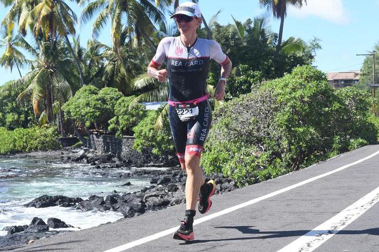Athlet in sportlicher Kleidung joggt entlang einer K&uuml;stenstra&szlig;e, umgeben von Palmen und dem Meer.