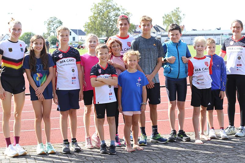 Gruppe von zehn Kindern und Jugendlichen in Sportkleidung steht auf einer Laufbahn im Freien.