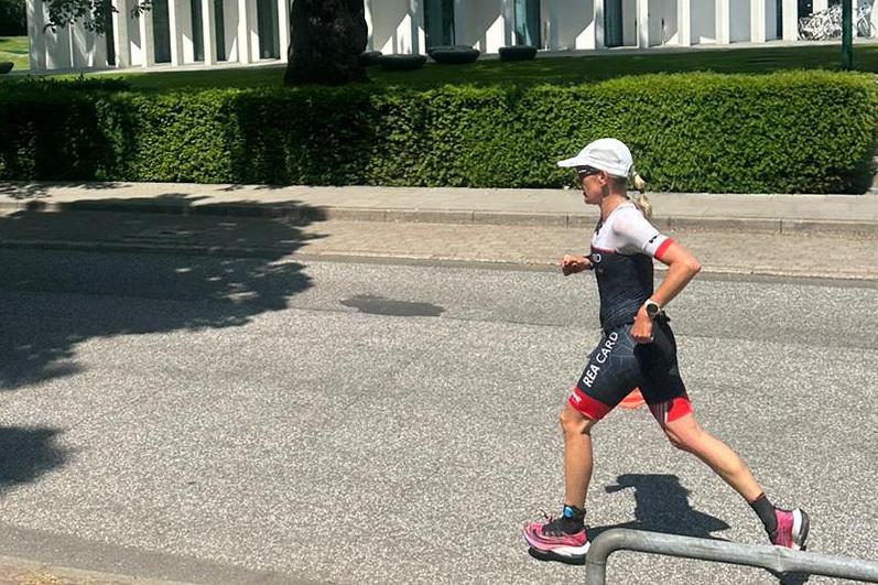 Frau in Sportkleidung läuft auf einer belebten Straße, im Hintergrund grüne Hecken und moderne Gebäude.