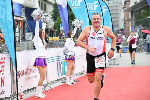 Mann im Wettkampfanzug sprintet auf roten Teppich, während Cheerleader jubeln und Fahnen wehen.