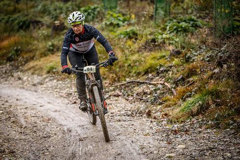 Mountainbiker auf einem schmalen, matschigen Pfad, trägt die Nummer 94 und steuert geschickt um Hindernisse.