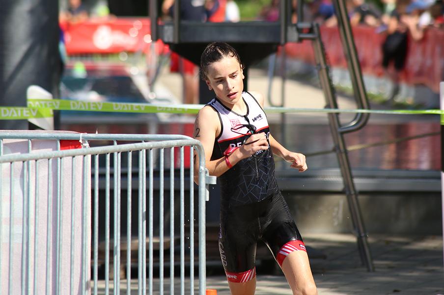 Junge Athletin in Sportkleidung läuft während eines Triathlons auf einer gepflasterten Strecke neben einem Wasserbecken.