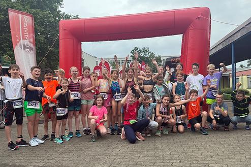 Gruppenfoto von Kindern nach einem Sportevent, vor einem roten Zielbogen, sichtbar fröhlich und jubelnd.