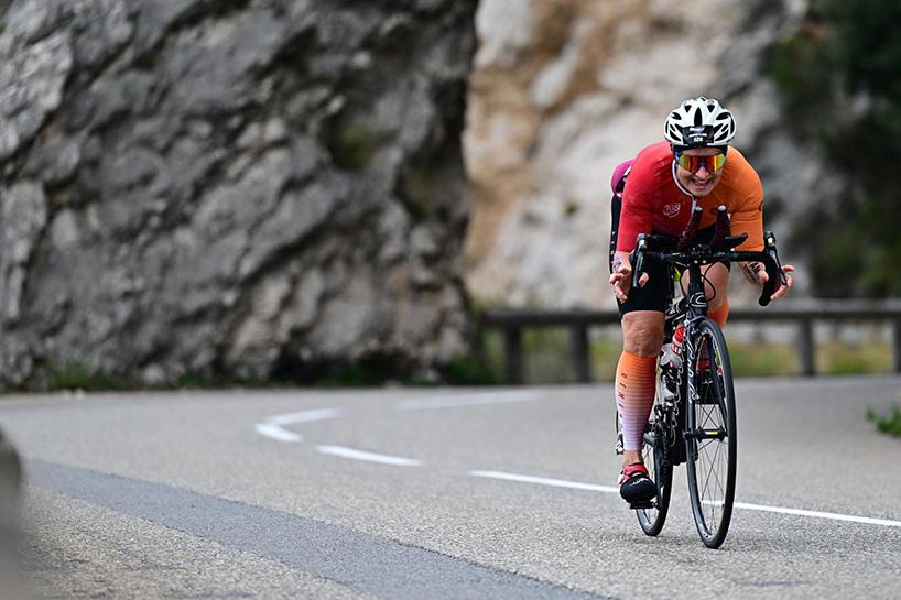 Eine Radfahrerin in buntem Outfit fährt auf einer kurvigen Straße durch eine felsige Landschaft.