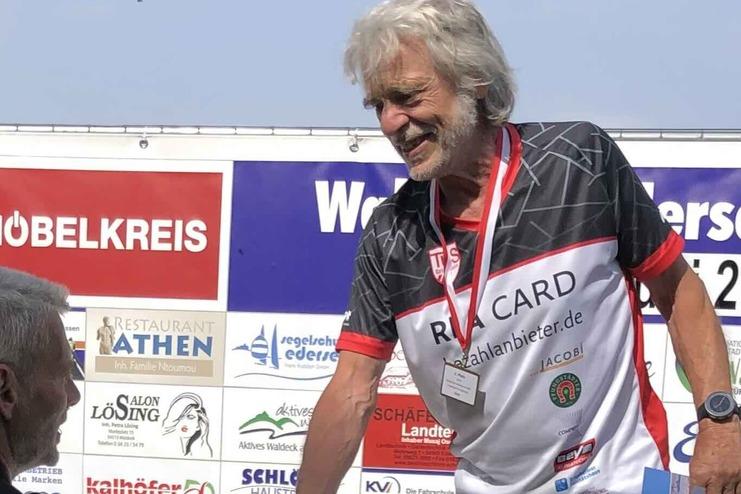 Ein &auml;lterer Athlet erh&auml;lt eine Medaille, w&auml;hrend er einem anderen Mann zum Sieg gratuliert auf einer Siegerb&uuml;hne.