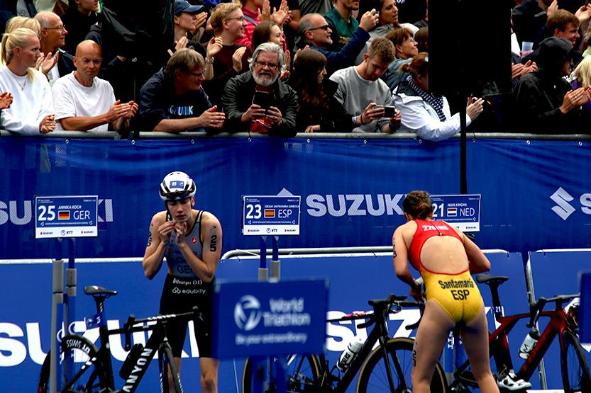 Zwei Triathletinnen bereiten sich auf den Wettkampf, umgeben von einem applaudierendem Publikum.