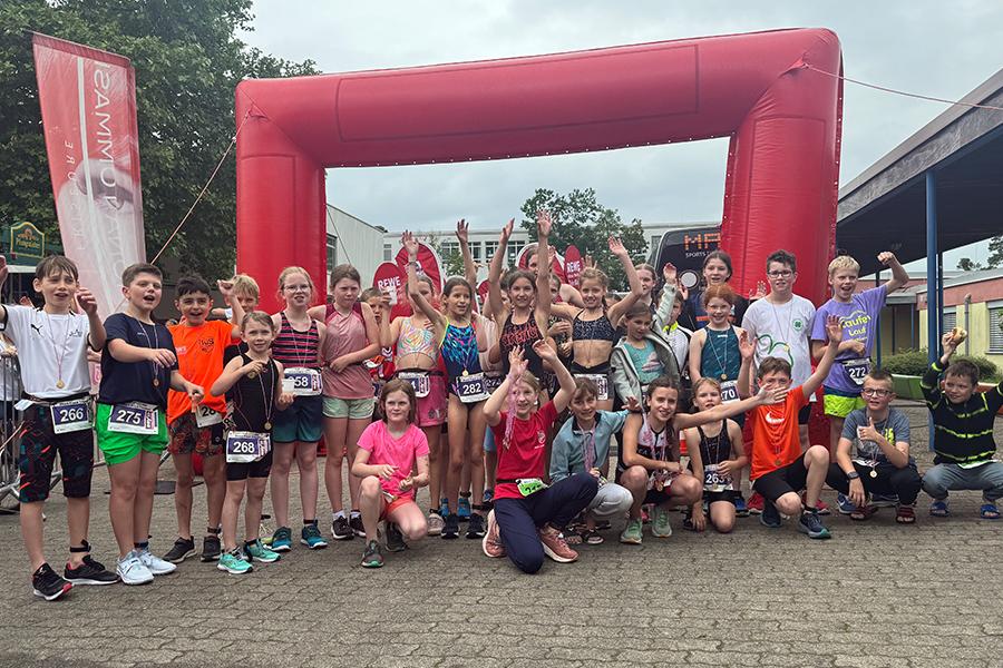 Gruppenfoto von Kindern nach einem Sportevent, vor einem roten Zielbogen, sichtbar fröhlich und jubelnd.