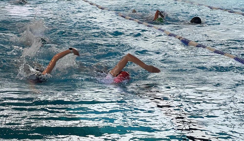 Schwimmerinnen im Wasser, die Wettkampfstarts im Rückenschwimmen auf einer Bahn im Schwimmbecken ausführen.