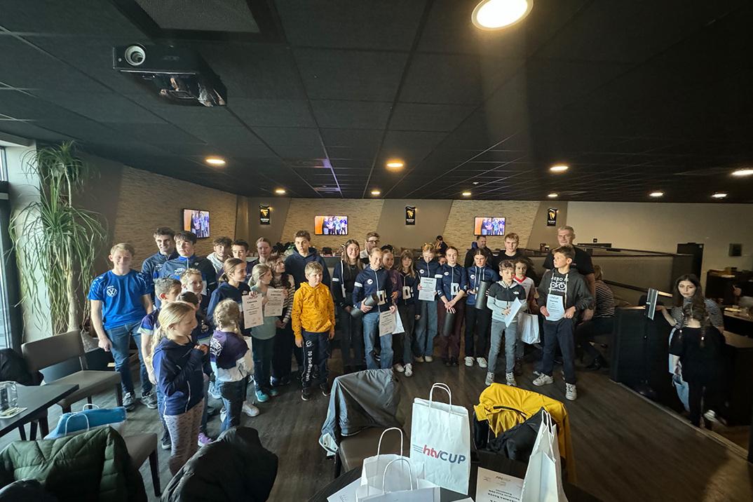 Gruppe von Kindern und Jugendlichen hält Zertifikate in einem Veranstaltungsraum mit Fernsehern im Hintergrund.