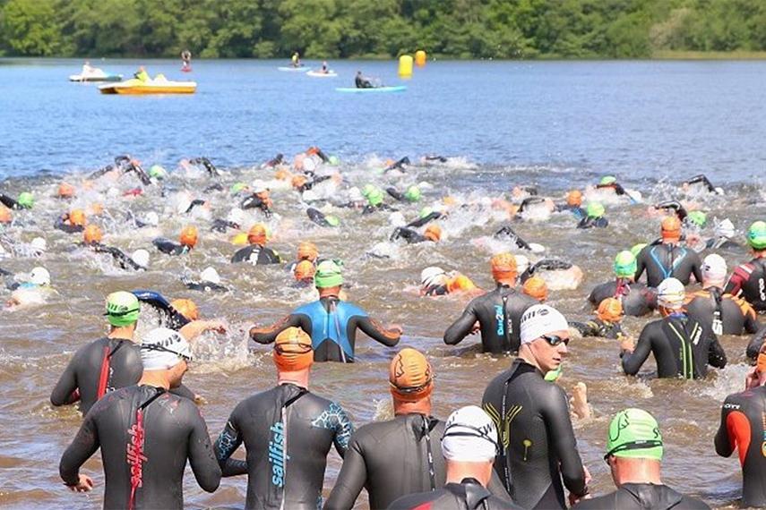 Gruppenszene von Schwimmern in Neoprenanzügen, die in einem See bei einem Wettkampf starten.