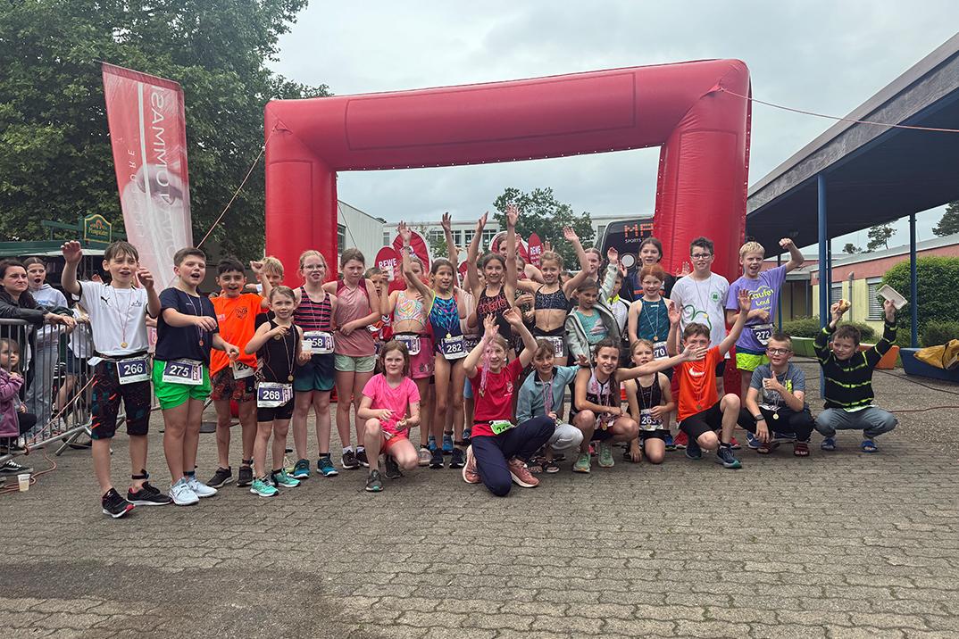 Gruppenfoto von Kindern nach einem Sportevent, vor einem roten Zielbogen, sichtbar fröhlich und jubelnd.