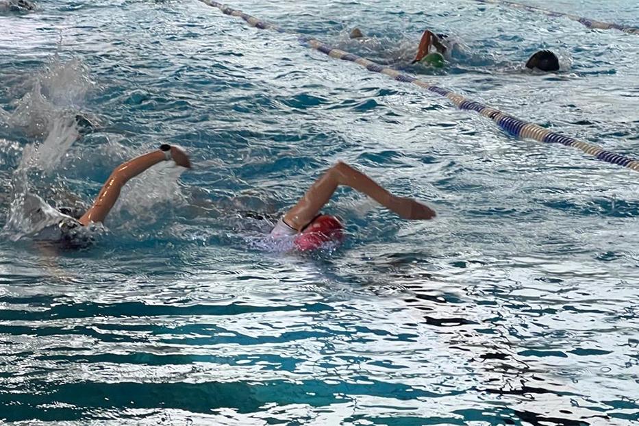 Schwimmerinnen im Wasser, die Wettkampfstarts im Rückenschwimmen auf einer Bahn im Schwimmbecken ausführen.