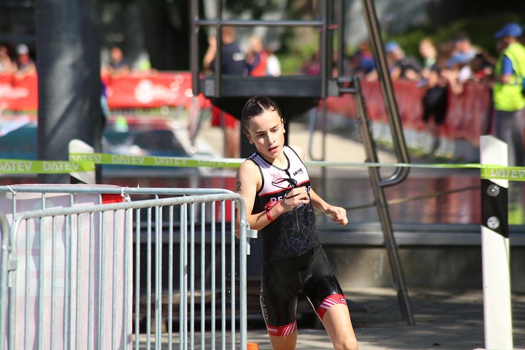 Junge Athletin in Sportkleidung läuft während eines Triathlons auf einer gepflasterten Strecke neben einem Wasserbecken.