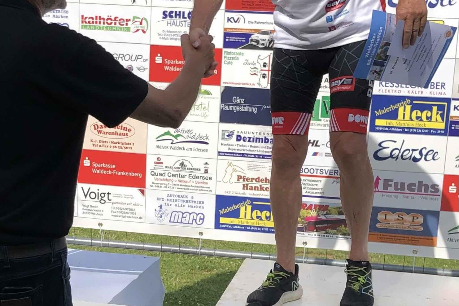 Ein älterer Athlet erhält eine Medaille, während er einem anderen Mann zum Sieg gratuliert auf einer Siegerbühne.