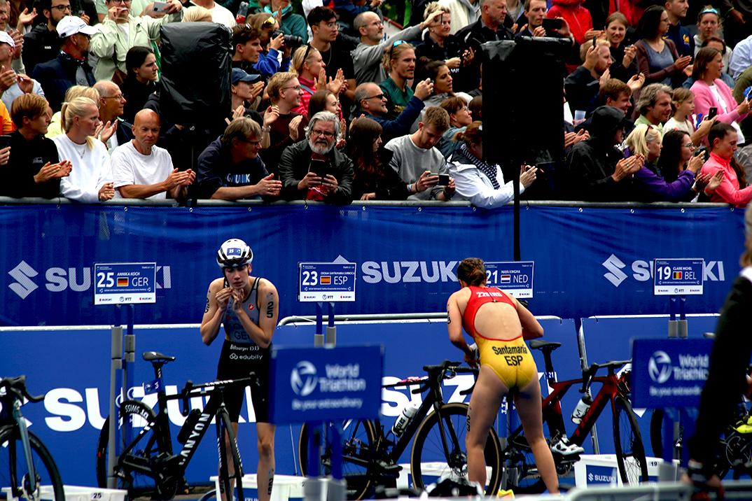 Zwei Triathletinnen bereiten sich auf den Wettkampf, umgeben von einem applaudierendem Publikum.