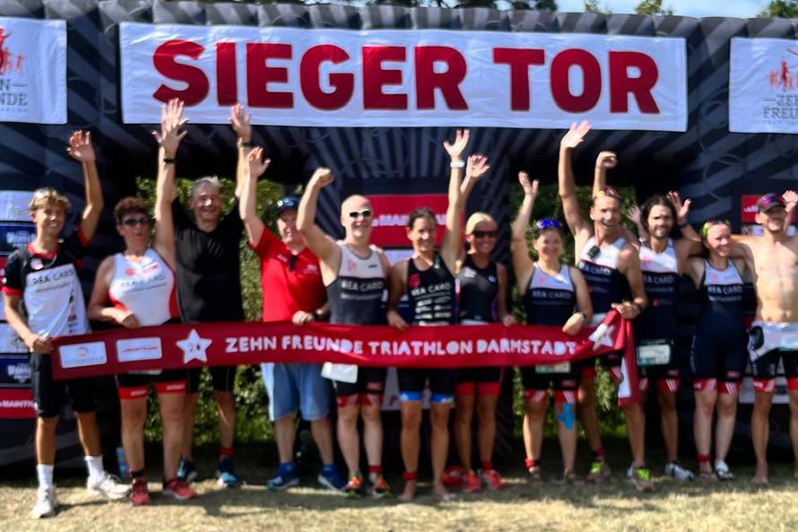 Gruppenfoto von Triathleten mit erhobenen Händen vor einem Siegerbogen beim „Zehn Freunde Triathlon Darmstadt“.