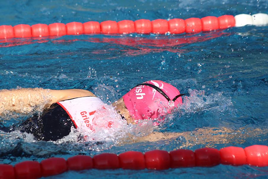 Schwimmerin in pinker Schwimmhaube zieht durch das Wasser, während sie an einem roten und weißen Schwimmbahn-Seil vorbeischwimmt.