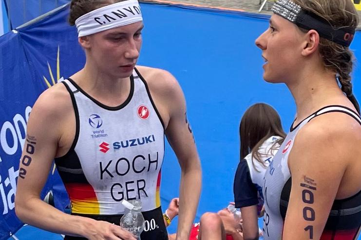 Zwei Triathletinnen im Gespr&auml;ch, eine h&auml;lt eine Wasserflasche, beide in sportlicher Bekleidung mit deutschen Nationalfarben.