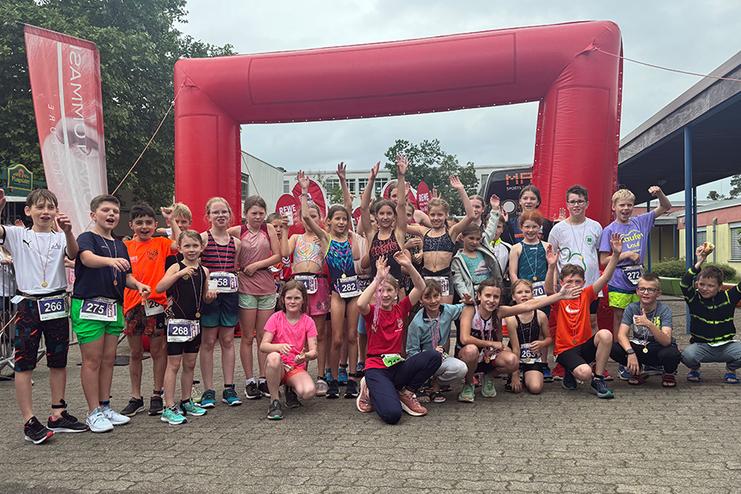 Gruppenfoto von Kindern nach einem Sportevent, vor einem roten Zielbogen, sichtbar fr&ouml;hlich und jubelnd.