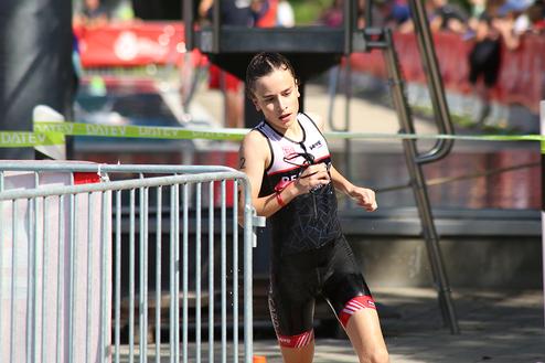 Junge Athletin in Sportkleidung läuft während eines Triathlons auf einer gepflasterten Strecke neben einem Wasserbecken.