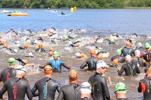 Gruppenszene von Schwimmern in Neoprenanzügen, die in einem See bei einem Wettkampf starten.