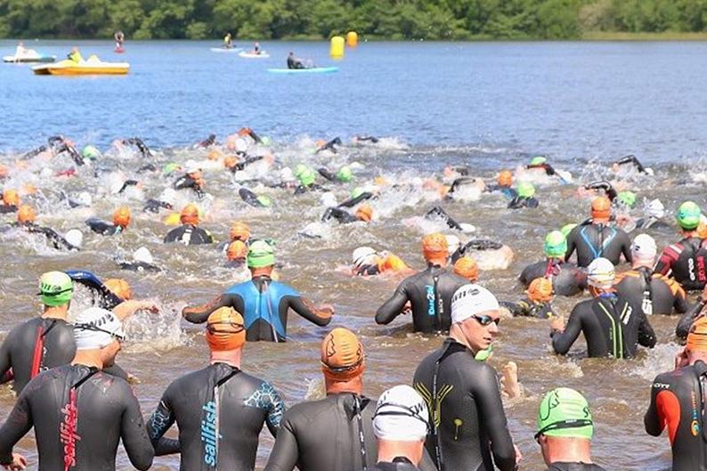 Gruppenszene von Schwimmern in Neoprenanzügen, die in einem See bei einem Wettkampf starten.