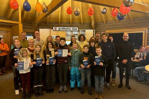 Gruppenbild von Teilnehmern einer Triathlon-Veranstaltung mit Urkunden und Pokalen in festlich dekoriertem Raum.