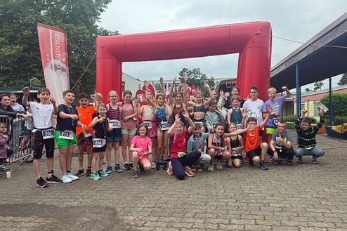 Gruppenfoto von Kindern nach einem Sportevent, vor einem roten Zielbogen, sichtbar fröhlich und jubelnd.