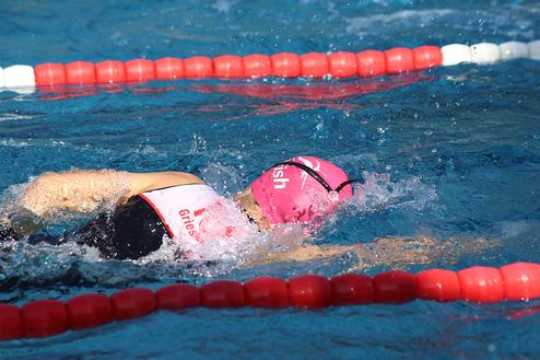 Schwimmerin in pinker Schwimmhaube zieht durch das Wasser, während sie an einem roten und weißen Schwimmbahn-Seil vorbeischwimmt.