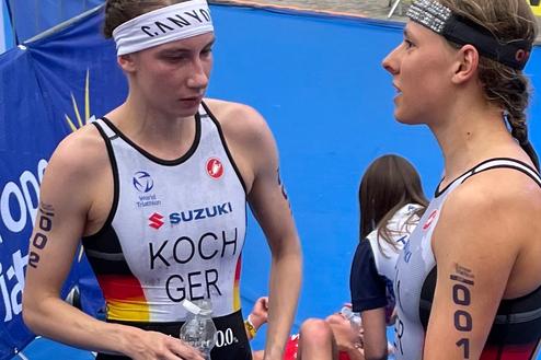 Zwei Triathletinnen im Gespräch, eine hält eine Wasserflasche, beide in sportlicher Bekleidung mit deutschen Nationalfarben.