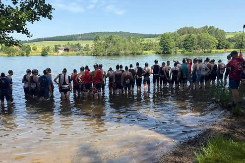 Gruppierung von Schwimmern im Wasser vor einer landschaftlichen Kulisse, bereit für einen Wettkampf oder Training.