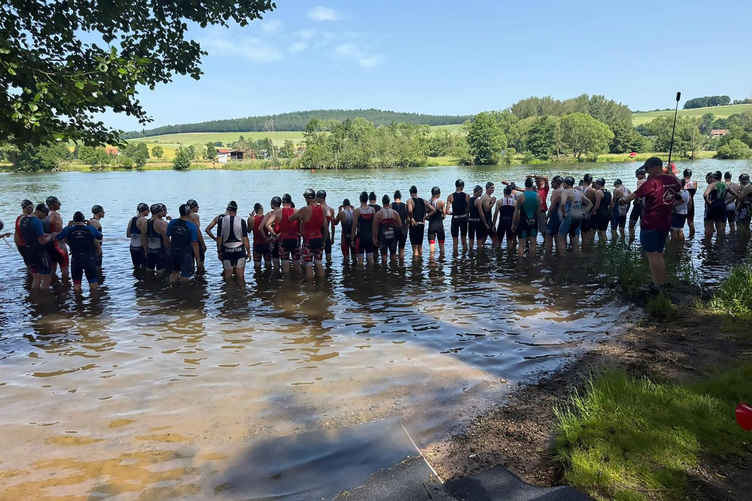 Gruppierung von Schwimmern im Wasser vor einer landschaftlichen Kulisse, bereit für einen Wettkampf oder Training.
