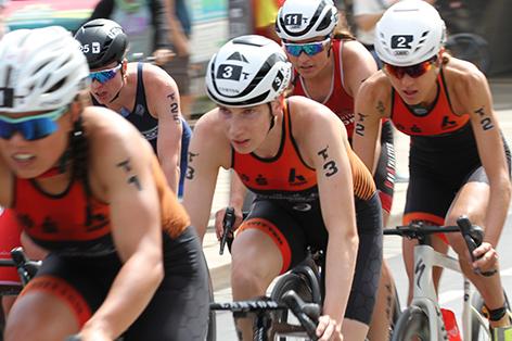 Fünf Athletinnen in Radfahroutfits absolvieren ein Rennen, Höhepunkt des Wettbewerbs mit Publikum im Hintergrund.