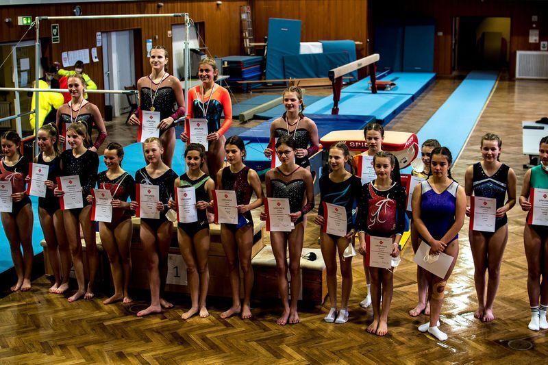Gruppe junger Turnerinnen in Wettkampfanzügen hält Urkunden und Medaillen in einer Turnhalle.