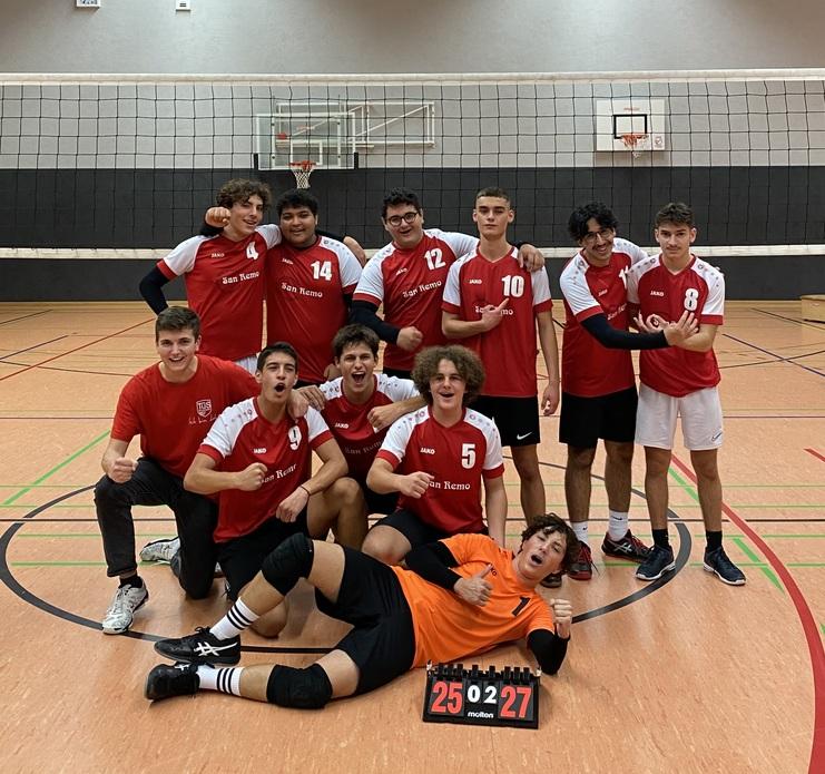 Gruppenvorstellung eines volleyballspielenden Teams in roten Trikots, sie feiern mit einem Punktestand von 25-27.