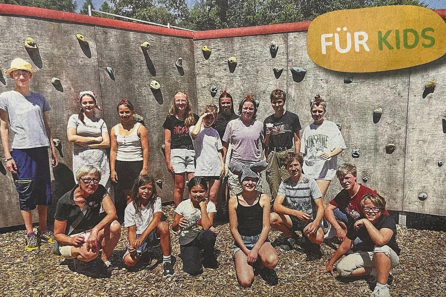 Gruppe von Kindern und Jugendlichen vor einer Kletterwand im Freien, einige lächeln in die Kamera.